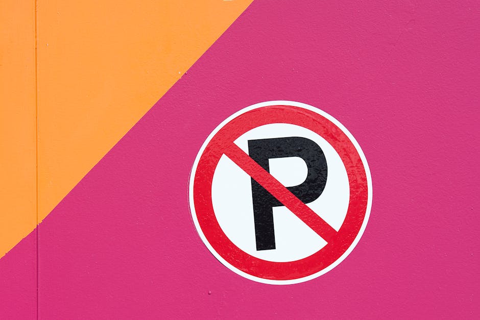 Close-up of a round no parking sign mounted on a colourful pink and orange wall. The sign features a bold black letter 'P' within a white circle, overlaid with a red diagonal slash indicating parking restriction. The wall's textured surface is painted in bright, contrasting shades, highlighting the sign's visibility for drivers. This image relates to parking restrictions that can impact house removals and moving logistics in Southfields, as temporarily unavailable parking may affect the load and unload process. Man with Van Southfields advises clients to be aware of such regulations during home relocation or furniture transport, ensuring smooth loading and unloading of boxes, furniture, and appliances. The image illustrates the importance of checking local parking rules before scheduling a moving day to avoid fines or delays, especially in areas with commercial or residential parking suspensions, relevant to the context of Southfields parking suspensions and removal services.